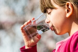 A girl drinking water from a glass cup.
