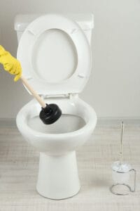 Person using a plunger to unclog a toilet bowl in a bathroom